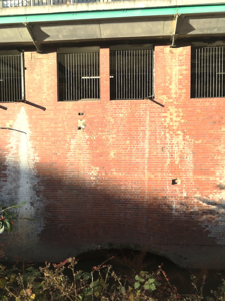 Photo of the visible entrance of the Duke’s Tunnel on the River Medlock, from a car park off Hulme Street